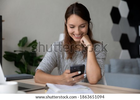 Distracted from study smiling millennial woman looking at smartphone screen, watching funny video photo or communicating distantly in social network, using mobile applications, break pause concept.