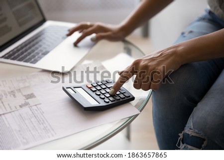 Close up young woman using calculator and online banking application on computer managing monthly expenditures, summarizing household utility bills or mortgage loan payments, bookkeeping at home. Royalty-Free Stock Photo #1863657865
