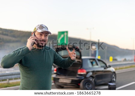 A man on the phone calls for help on the road. Problem with the car on the road.