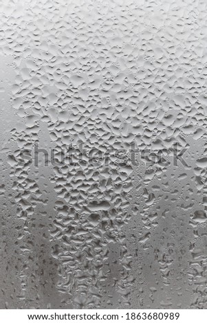Close up water drop on grey background, misted glass with droplets of water draining down. Dripping Condensation