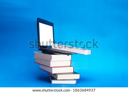 Laptop and stack of assorted books on blue background
