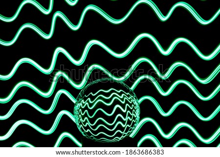 Long exposure photograph of neon green colour in an abstract ripple, parallel lines pattern against a black background with reflections in a glass orb. Light painting photography.