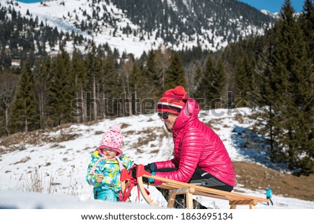 Mother and daughter sledging across fresh snow covered slopes.