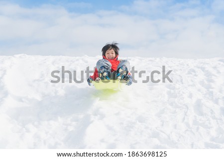 Cute Asian child sliding on sleds down snow hill in winter,Hokkaido japan