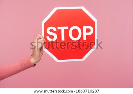 Side view closeup female hand in pink sweater holding and showing stop warning sign, domestic violence victim. Indoor studio shot isolated on pink background
