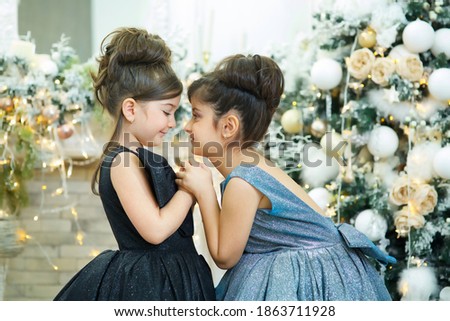 Two baby girl in festive attire is in the room decorated for the new year and Christmas. The concept of holidays and gifts.