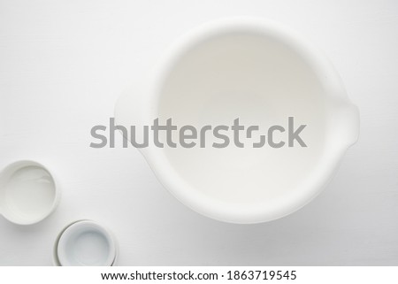 Large white plastic bowl for the dough and containers for ingredients on a light background. Top view of preparation for cooking