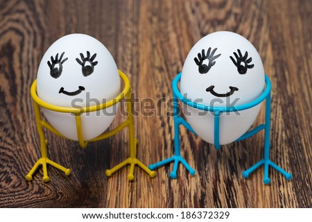 two funny smiling eggs on stands on a wooden background, close-up