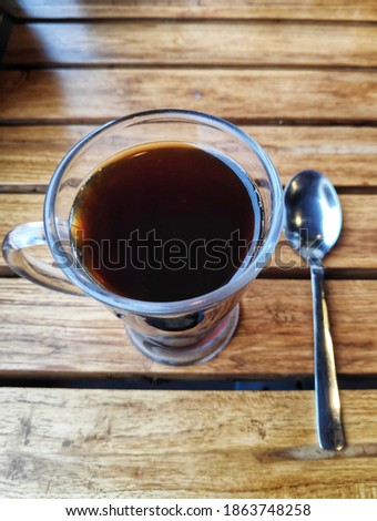 espresso black tea coffee in a transparent glass cup with a tea spoon on a wooden table high angle shot