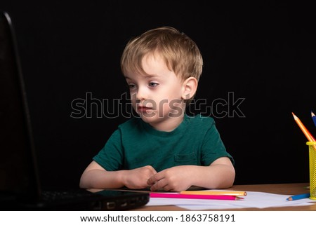 A little three-year-old boy sits at a table with books and a laptop. distance learning during quarantine. child does homework. European appearance