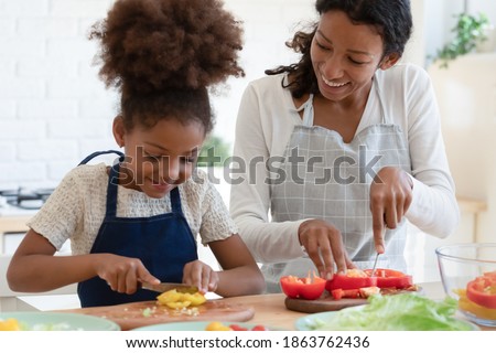 Culinary is easy. Inspired happy african american mother and tween daughter prepare vegan food, grown elder and small younger sisters trying new cooking recipe, cutting vegetables talking at kitchen Royalty-Free Stock Photo #1863762436