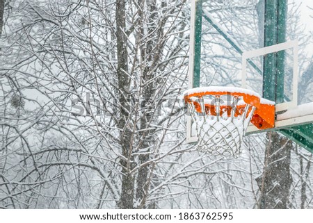 Close up shot of a basketball basket on a playground in a park covered with snow during a snowfall in winter. Natural snowy winter background.  