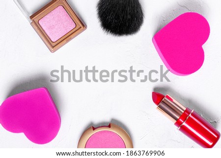 Cosmetics background. Make up brush, heart shaped sponge, red lipstick, pink eyeshadows and blusher on white. Copy space in the middle