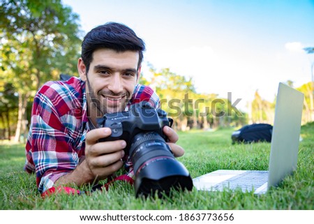 portrait of young business handsome man using dslr digital camera and take a photo with natural at public park. He has a bright smile and happiness. Ideas for work outside and relaxing in the garden