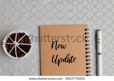 Top view of pen, dried flower and notebook written with text NEW UPDATE. Business and education concept. 