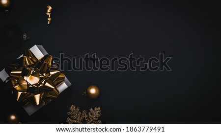 Holiday winter background. White gift box with golden ribbon, New Year balls and sparkling lights garland in Christmas composition on black for greeting card. Flat lay, top view, copy space.