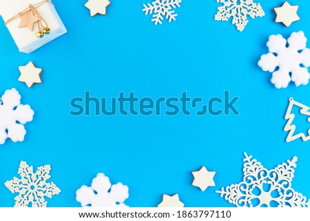 Flat layout of white package with Christmas gift and group of snowflakes surrounding copyspace for your greetings against blue background