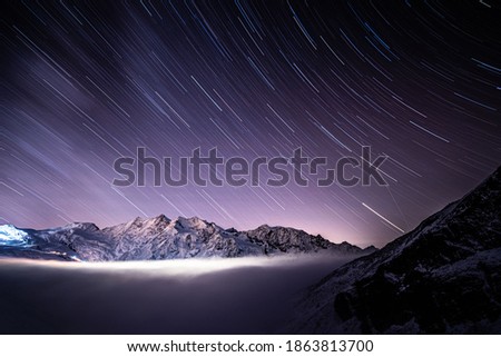 Above clouds with night sky star trails above Wallis mountains and Saas-Fee peaks, Alps, Switzerland, Europe