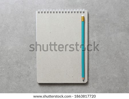 A spring notebook with a sheet of craft paper A5 with simple green graphite pencil on light grey concrete background. Concept of new idea, business plan and strategy, development and implementation of