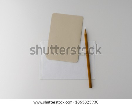 An empty kraft brown card for an invitation or greeting, a white paper envelope, and a yellow pencil on a white background. Layout. Stylized stock photos. The view from the top. Mock-up.
