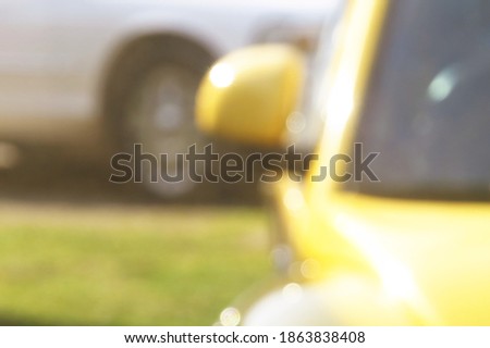 A purposefully blurry, unfocused background of a yellow car in the sunlight, a white car in the distance behind.