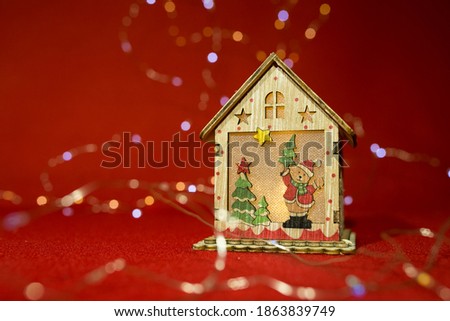 New Year and Christmas card on a red background. Wooden toy house and Christmas lights.