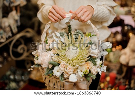 beautiful floral arrangement of white flowers and green spruce branches in white wicker basket in woman's hands