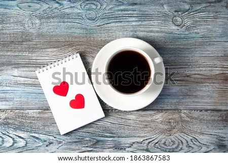 White coffee mug and two red hearts on a Notepad on a wooden background. The view from the top. The Concept Of Valentine's Day.
