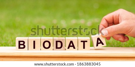 Word BIODATA written with wooden blocks. Man hand holding wooden cube block with BIODATA business word on green lawn background