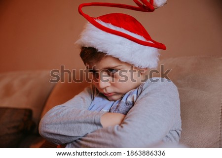 A close-up picture of an angry boy with blue eyes wearing a Santa hat