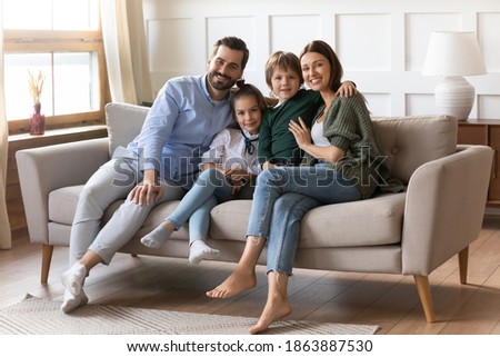 Portrait of happy young Caucasian family with two small kids sit relax on couch in new design living room. Smiling parents renters buyers with little children rest in own renovated home on weekend. Royalty-Free Stock Photo #1863887530