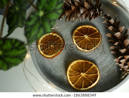
a flowerpot with a flower is on the windowsill, and cones, a dried orange and a garland are lying on a tray nearby