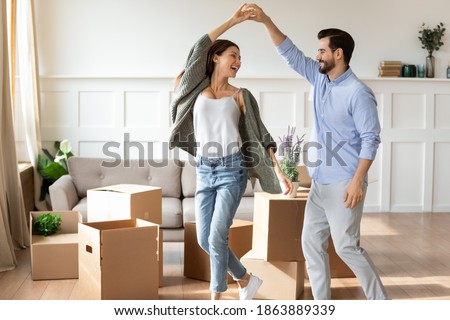 Overjoyed young Caucasian couple renters have fun excited moving in new home together. Happy man and woman tenants dance enjoy relocation day to own house. Relocation, real estate, rent concept. Royalty-Free Stock Photo #1863889339