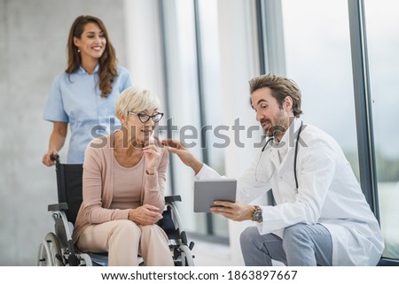 Successful doctor and young nurse talking with their senior female wheelchair-bound patient.