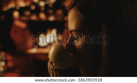 Beautiful romantic girl with cup of coffee or tea. Beautiful girl is enjoying coffee. Festive interior with lights, Christmas tree and fireplace in the background. Winter evening, cozy. Soft focus