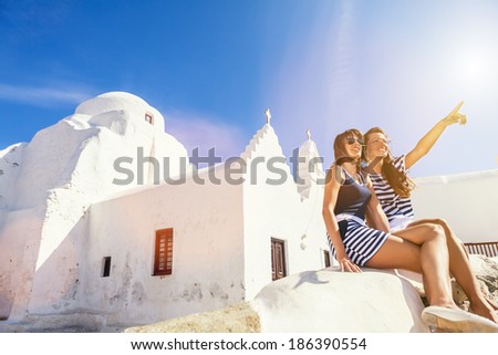 Young, excited women sitting in the front of the church, pointing at something. Flare light, Mykonos Greece, Greek architecture.