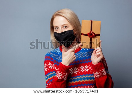 Beautiful blonde in Christmas sweater with a gift on gray background