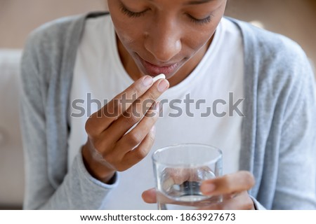 Crop close up of young African American woman feel unhealthy drink medicine with water. Unwell biracial female have pill or drug, take daily dose of vitamins or supplements. Healthcare concept. Royalty-Free Stock Photo #1863927673