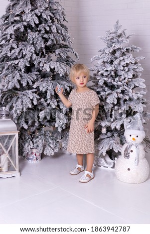 Cute little girl in a beautiful dress. Beautiful  girl posing near the christmas tree. Merry Christmas and Happy New Year. Snowman.
Christmas miracles. 