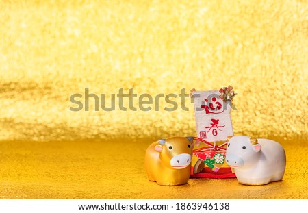 Japanese greeting Card with handwriting ideograms Geishun meaning Welcoming Spring on a washi paper and two cute Zodiacal animals figurines of cow for the Year of the Ox on a golden background.
