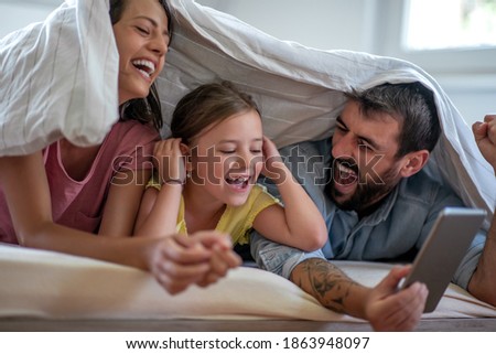 Love,happiness,fun and family concept.Happy mother, father and daughter with tablet on bed at home. 