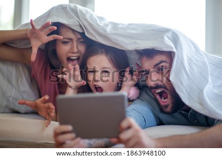 Love,happiness,fun and family concept.Happy mother, father and daughter with tablet on bed at home.