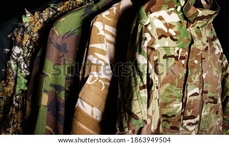 Photo of a hanging military camouflaged jackets on black background.