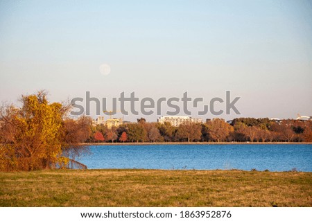 Image of lake with moon and buildings in distance. 