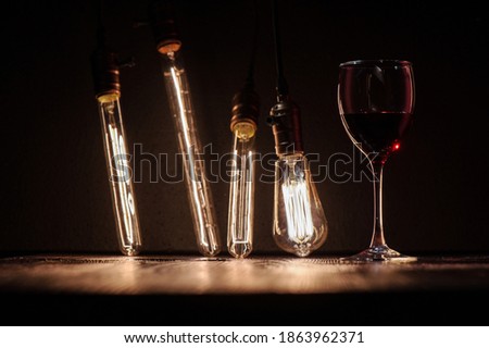 wine glass with wine on a dark wooden table against the background of an edison lamp