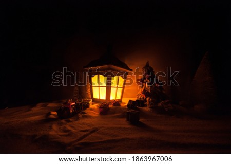Christmas lantern on snow with fir tree and moon. Festive dark background. New Year's still-life postcard lamp covered in snow with glowing candle at night. Holiday concept. Artwork