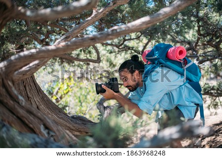 Male photographer with a camera on a hike. Young handsome guy with a backpack and a professional camera takes pictures of nature on a hike among the trees in the mountains
