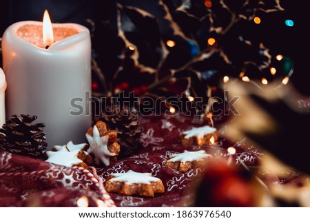 Christmas background composition on rustic table and fairy lights bokeh, setup made of gingerbread stars and candles on pink cloth, christmas messy table arrangement with candle fire in dark room