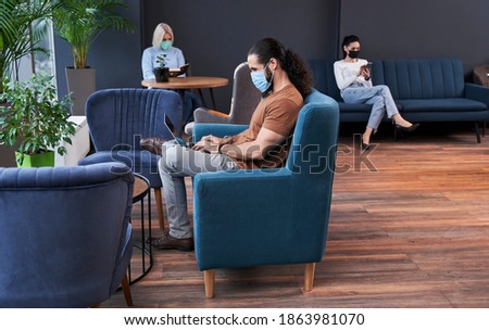 Three coworker people sitting at the safe distance from each other while working together at the modern office during pandemic. Stock photo