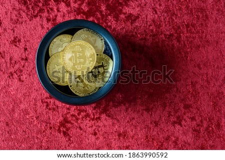 Gold bitcoins in a black pot on a red background
